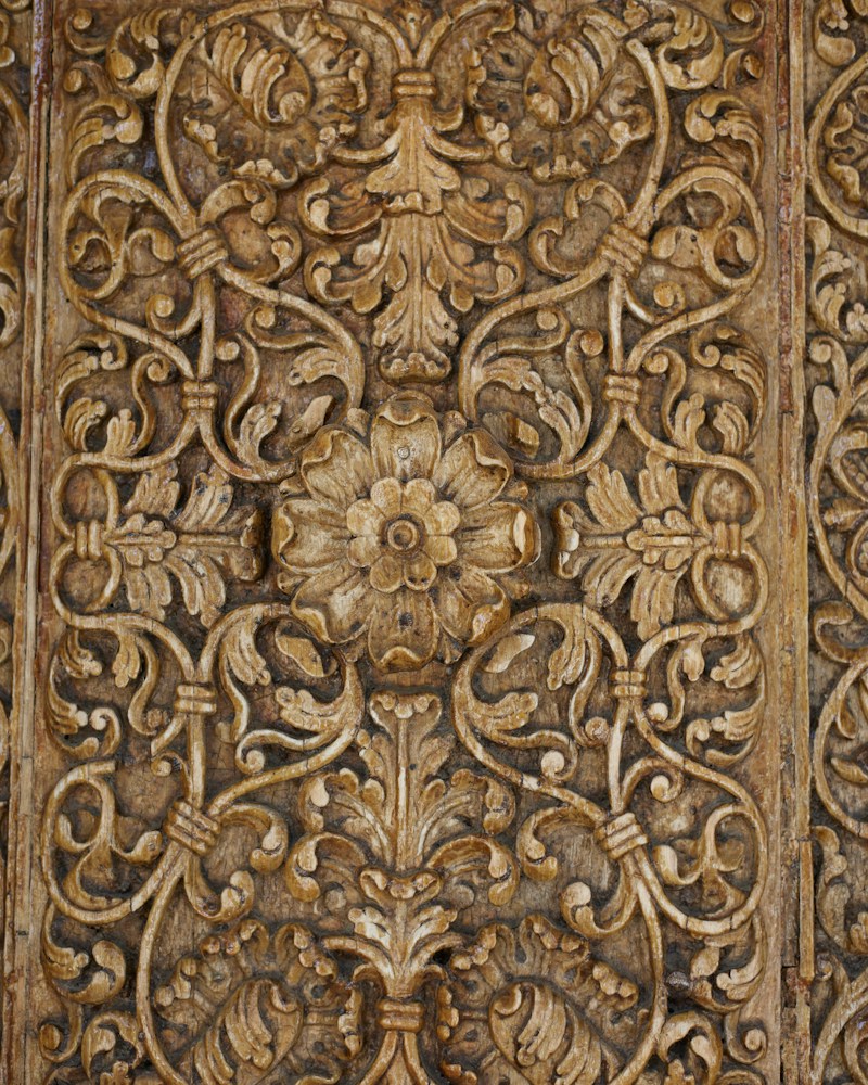 Intricate floral carvings on a weathered wooden panel with scrolling vines