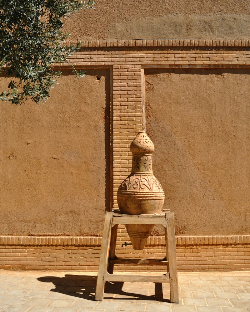 Ornate terracotta clay pot on a stand against a textured wall