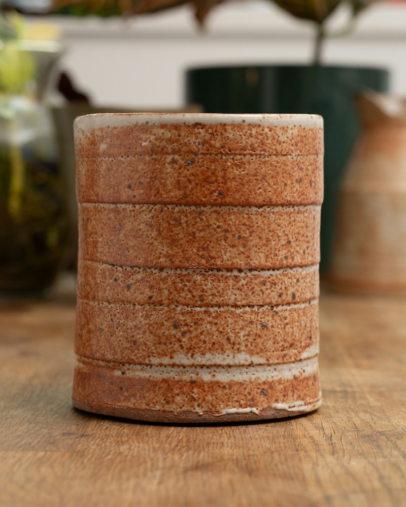 Rustic ceramic pot with textured bands on a wooden surface