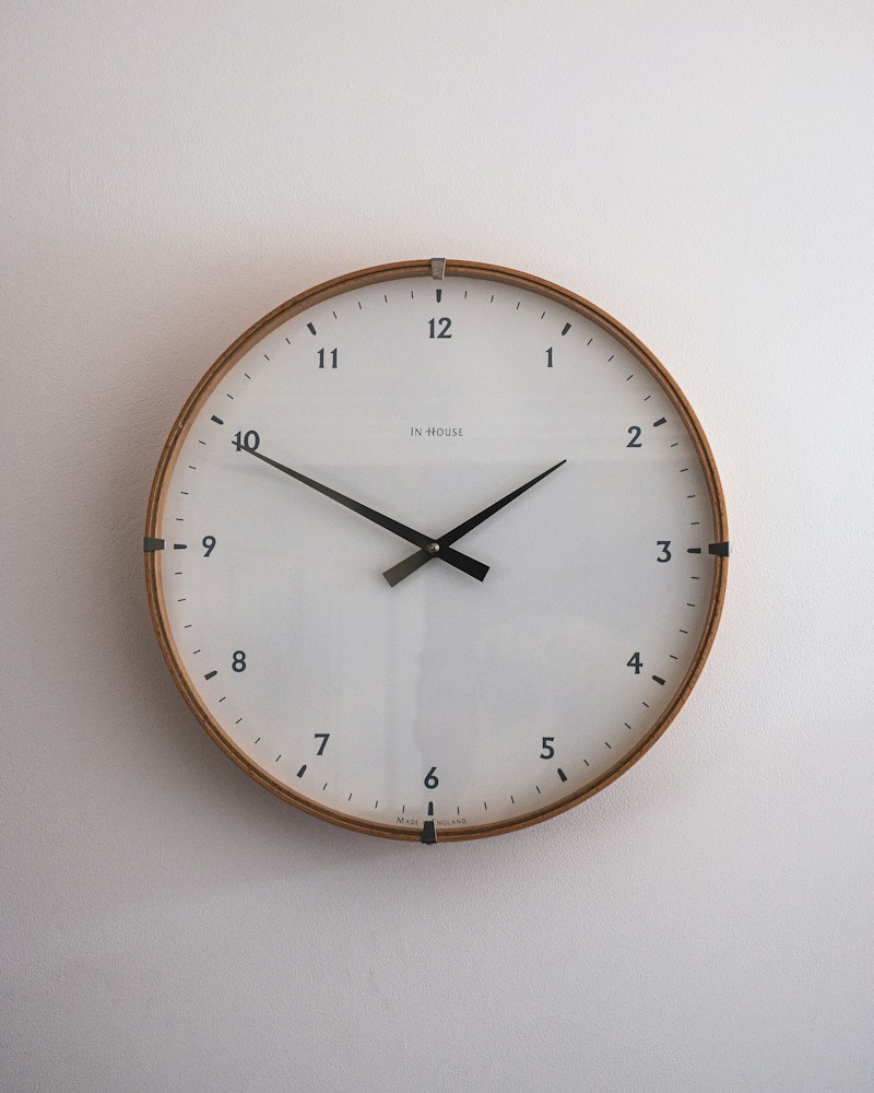 Minimal round wall clock with thin brass hands on a light background