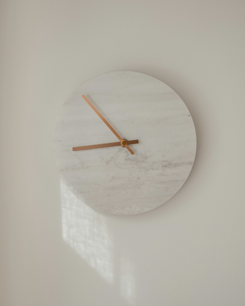White minimal analog wall clock hung against a clean wall